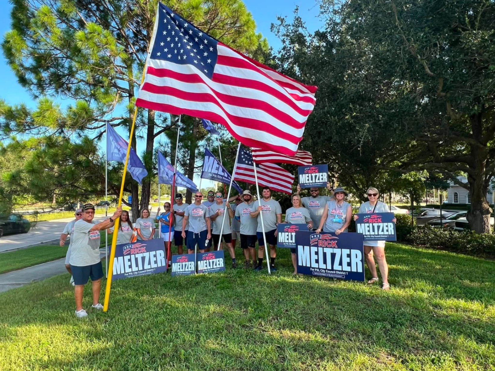 Volunteers holding Meltzer signs and American flags in a park